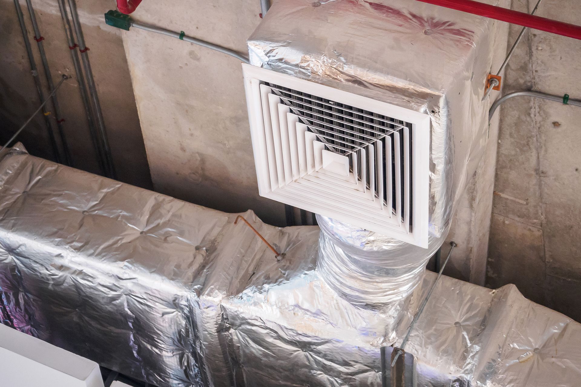 Wrapped HVAC duct with square vent opening in an unfinished wall, covered in reflective insulation.