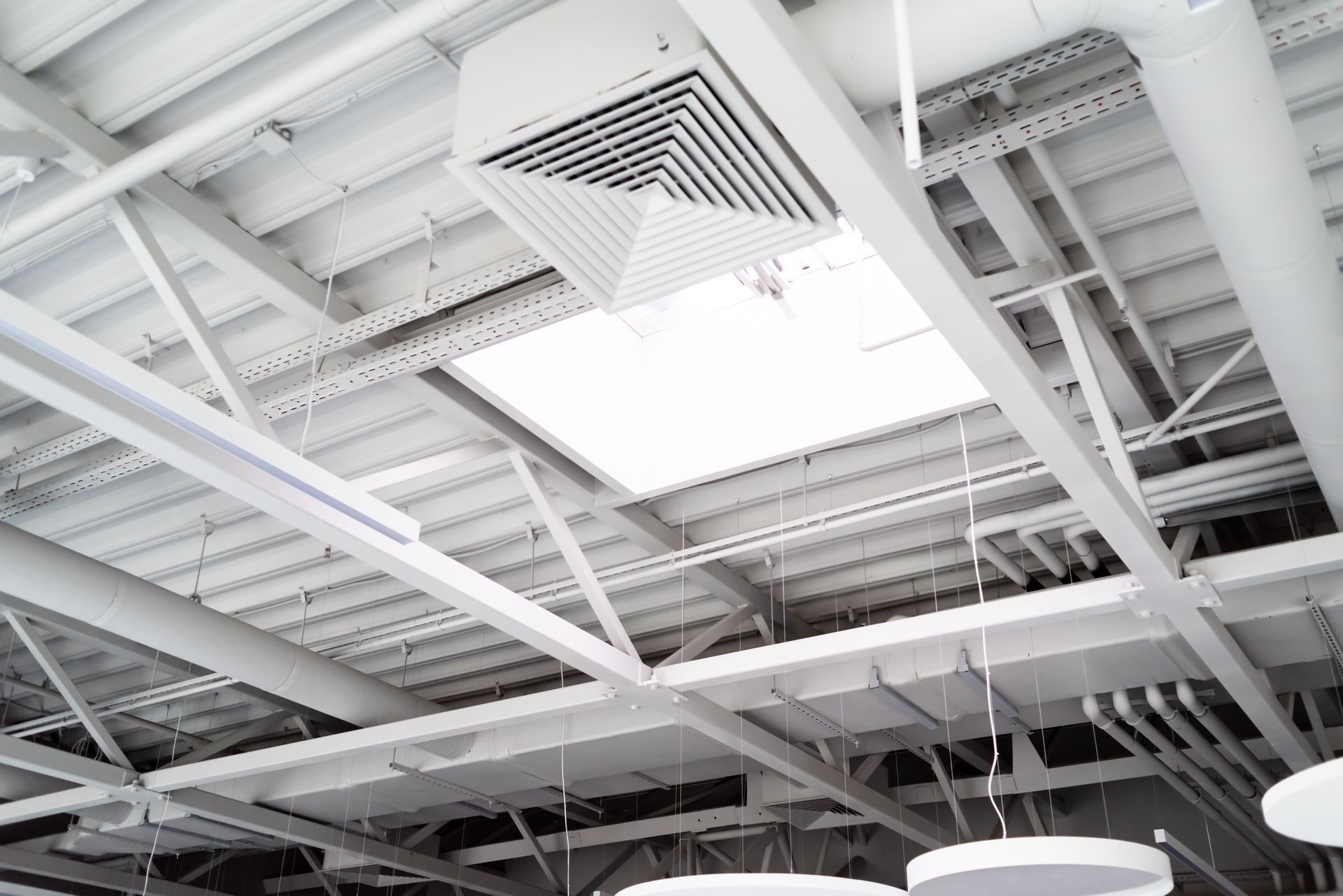 Industrial ceiling with white beams, ducts, and vents in a bright indoor space