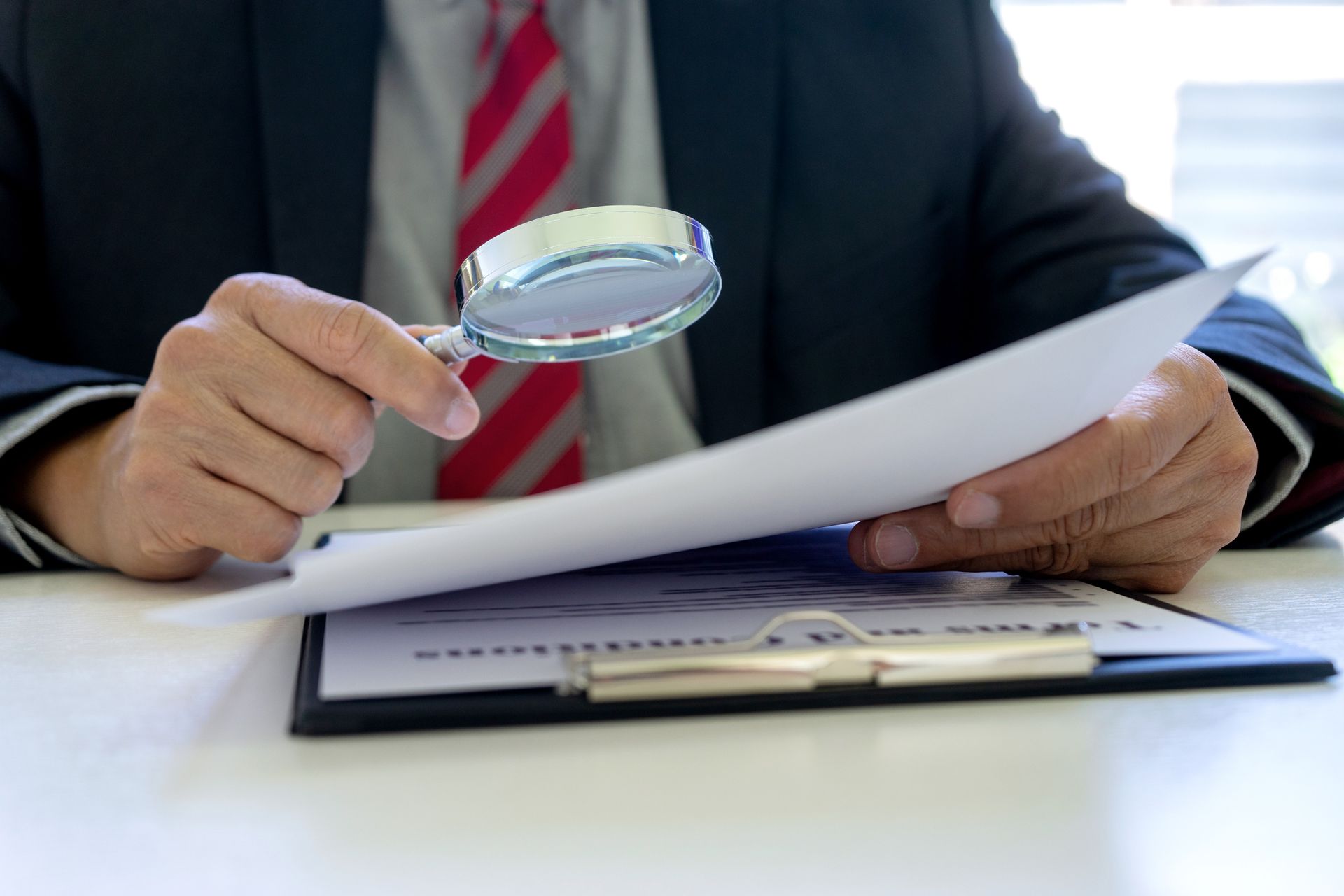 A man in a suit and tie is holding a magnifying glass over a piece of paper.