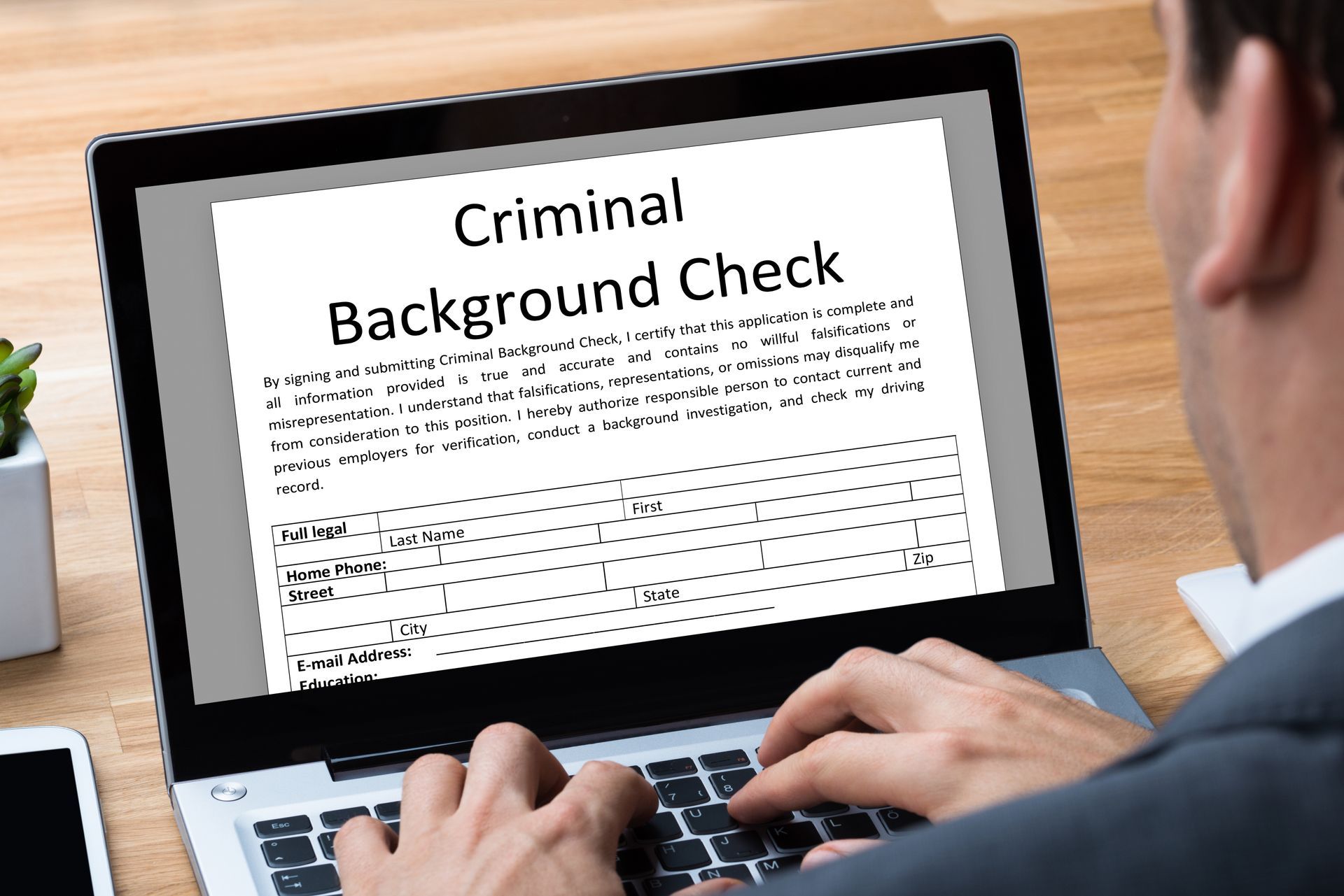 A man is typing on a laptop computer with a criminal background check on the screen.