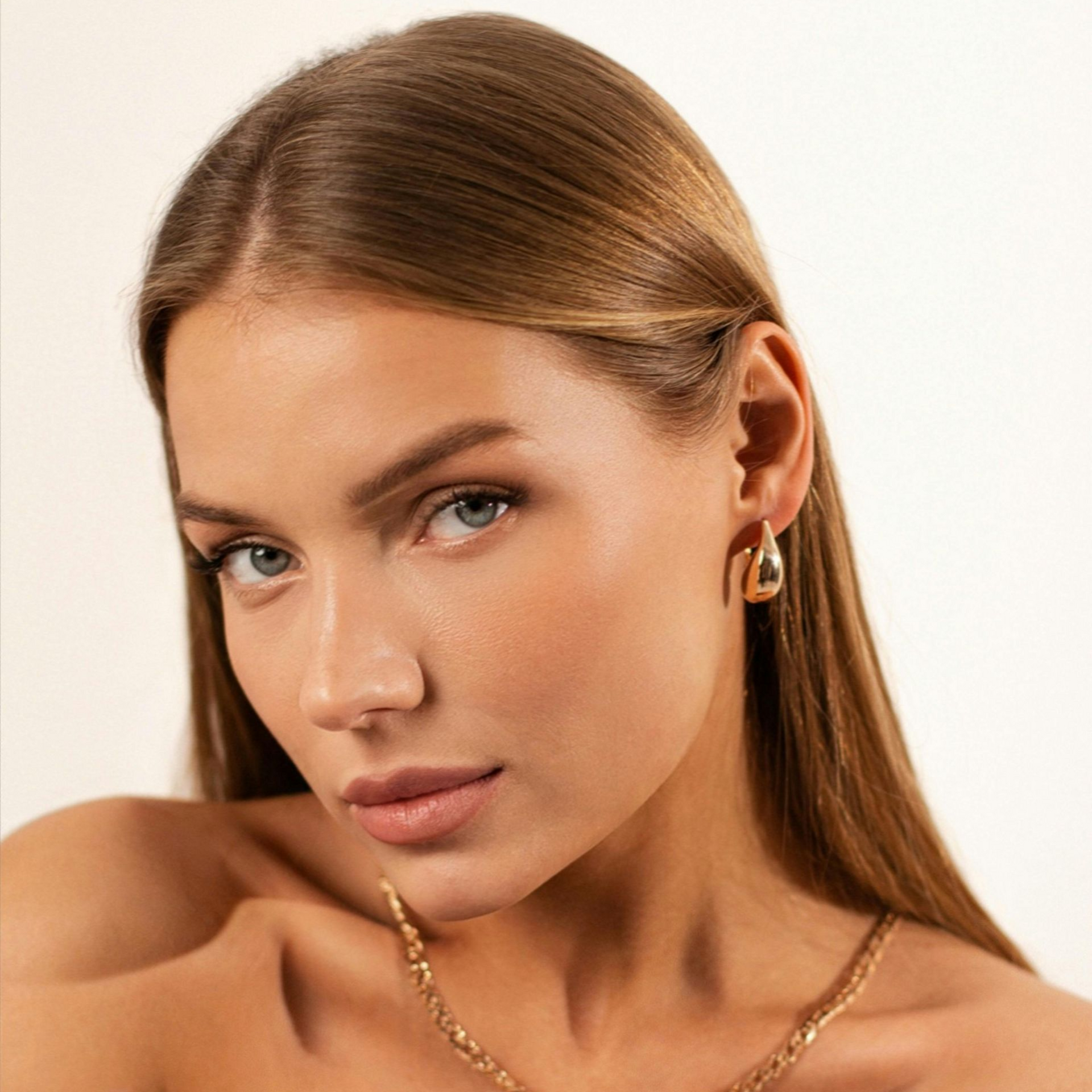 Primer plano de una mujer de piel morena, con pendientes de oro, mirando directamente al espectador.
