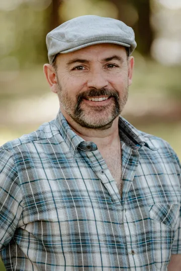A man with a beard is wearing a plaid shirt and a hat.