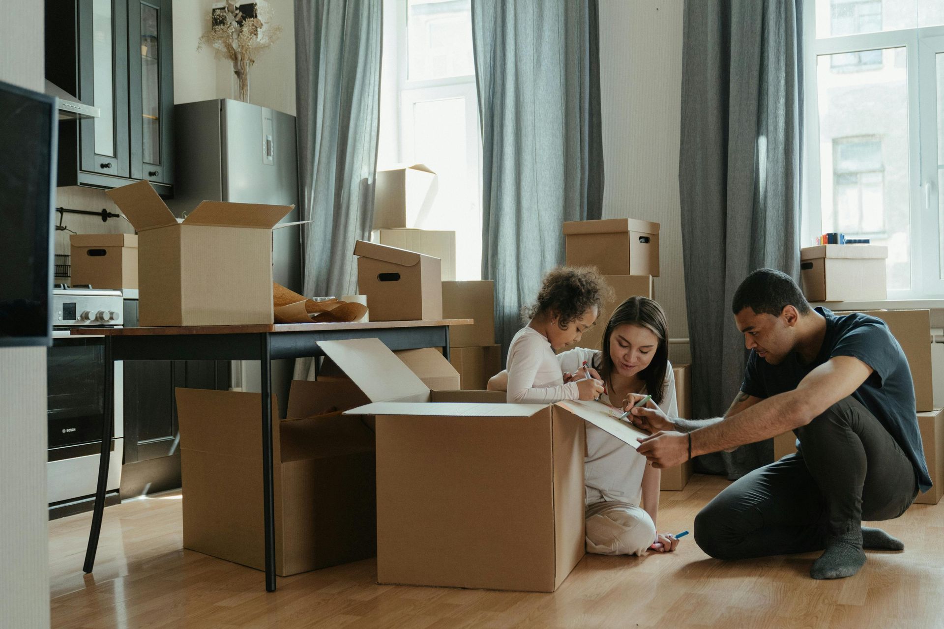 Family unpacking boxes in a bright living room with a toddler on the floor