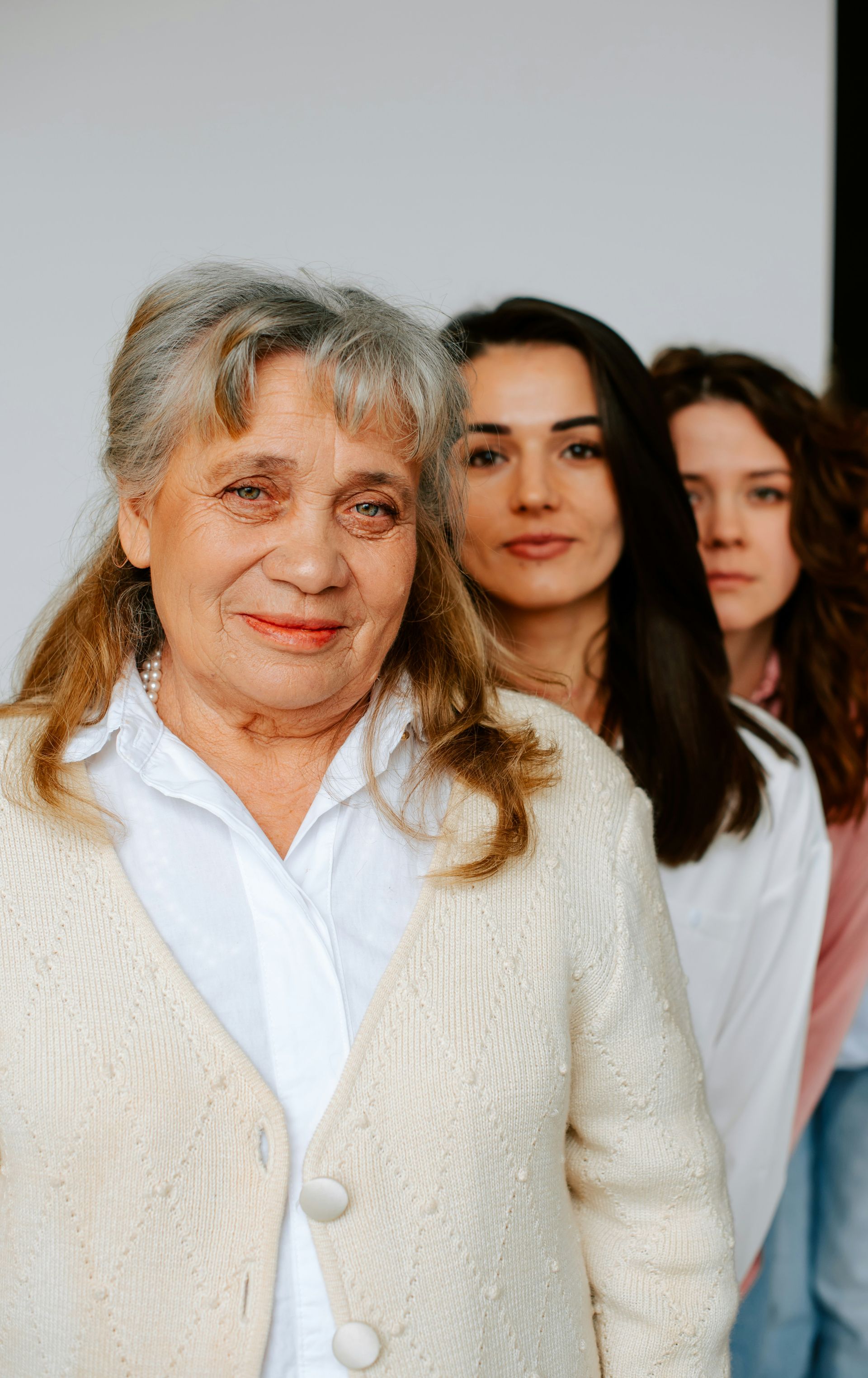 Three people stand in a line against a plain white background, each looking toward the camera.