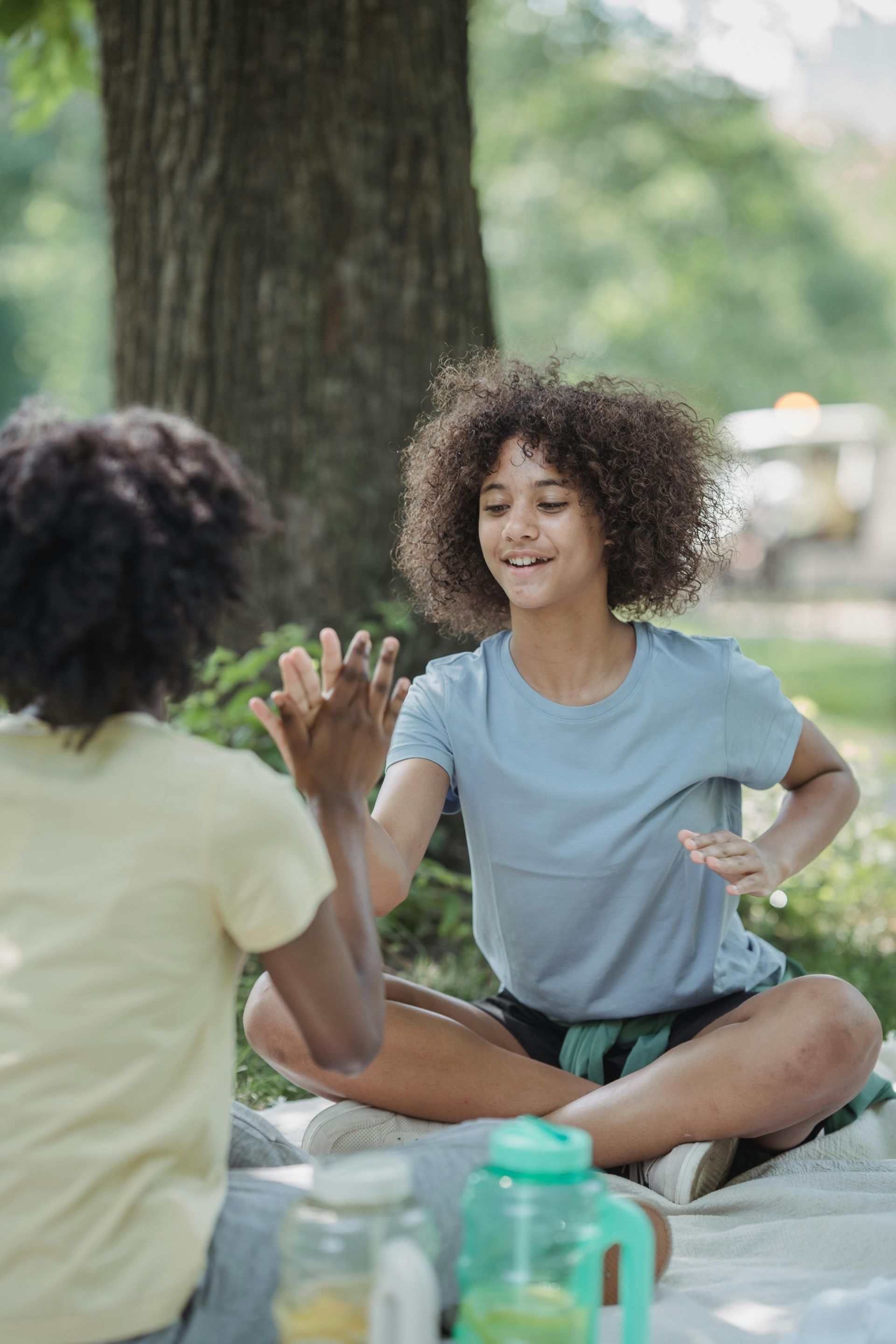 Two people sitting on the grass in a park, clapping their hands together and smiling.