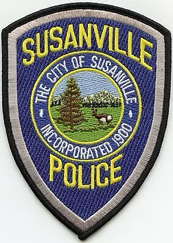 The Susanville Police department patch is a blue shield featuring a central circular logo of a tree, deer, and mountains.