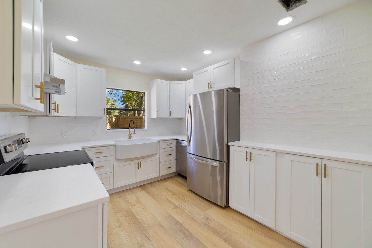 White kitchen with stainless steel appliances, light wood floor, and white cabinets.