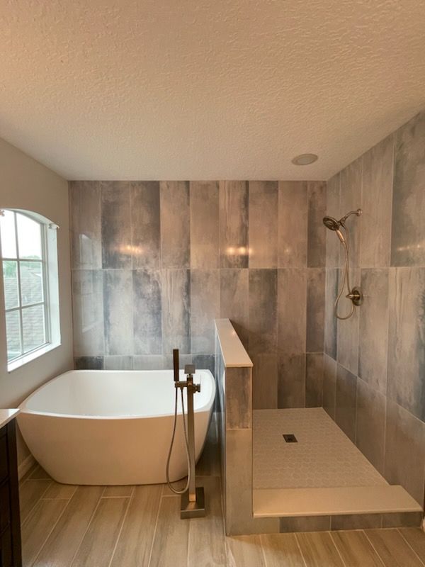 Modern bathroom with a freestanding tub and a walk-in shower, featuring gray-blue tiled walls and a light wood floor.