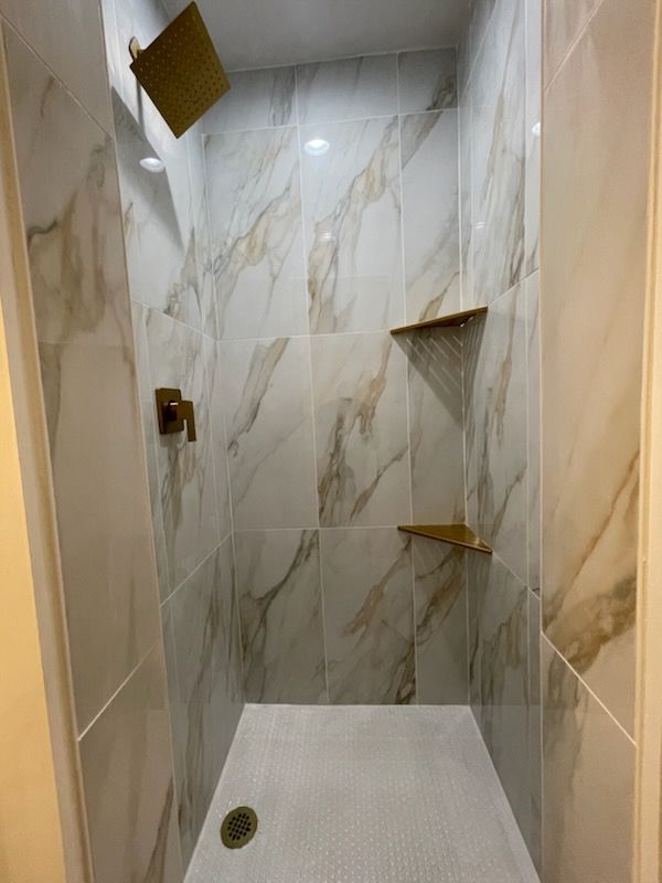 Modern shower with gold fixtures, marble-look tiles, and built-in shelves.