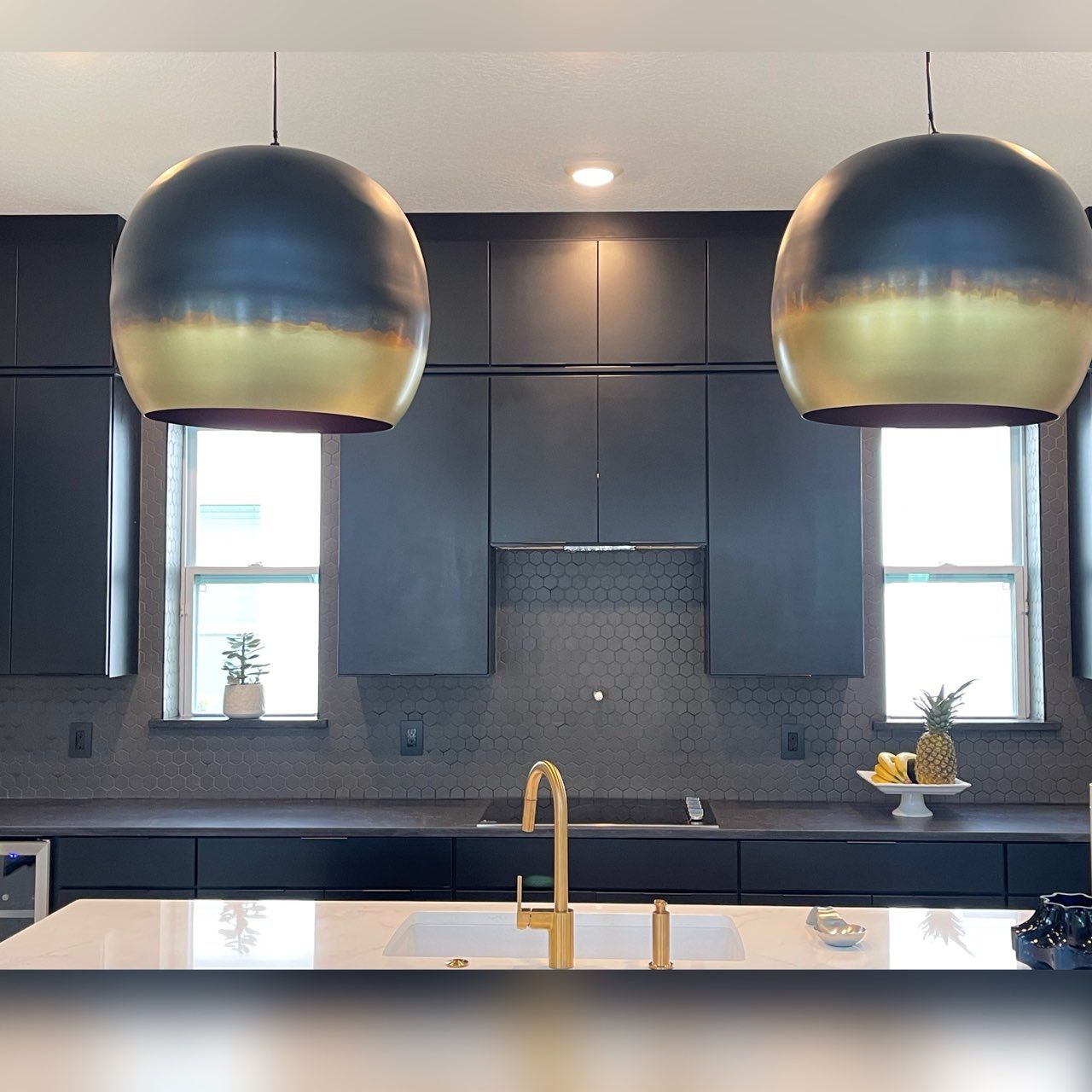 Modern kitchen with black cabinets, gold fixtures, white countertops, and two gold-rimmed pendant lights.