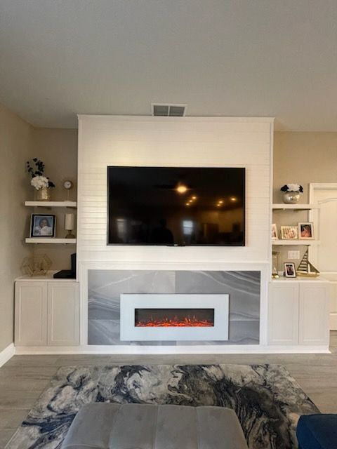 Living room with TV above fireplace, flanked by shelves and cabinets, neutral tones.