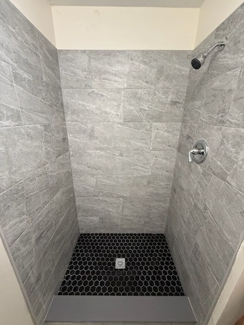 Gray tiled shower with black hexagon tile floor and silver fixtures.