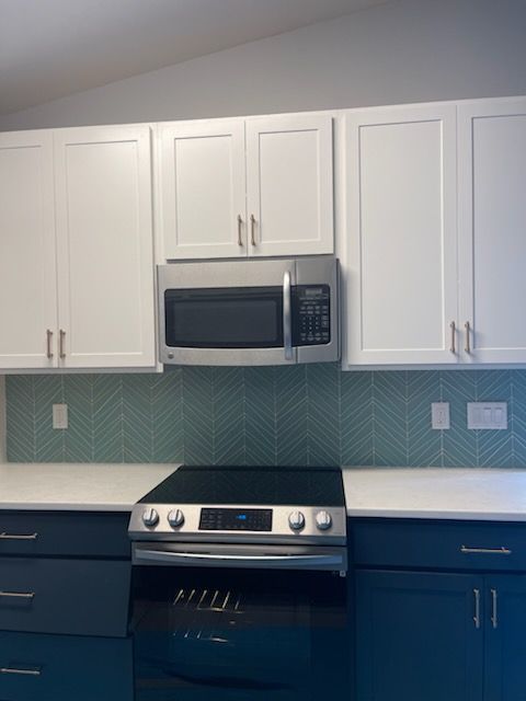 Kitchen with blue and white cabinets, stainless steel microwave, stove, and teal tile backsplash.