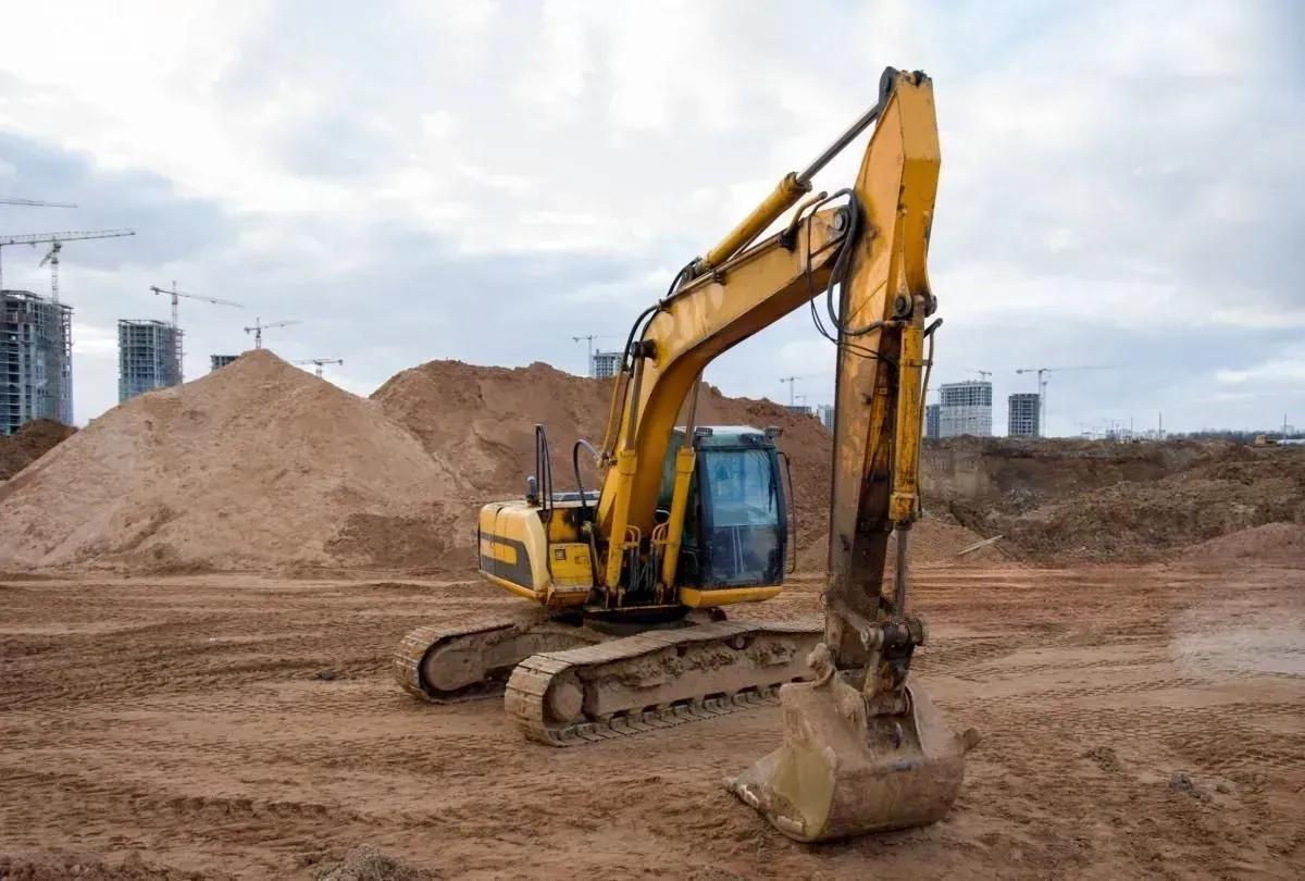 Yellow excavator working on a dirt construction site with piles of earth in the background