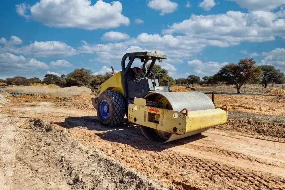 Yellow road roller on a dirt road under a blue sky with clouds