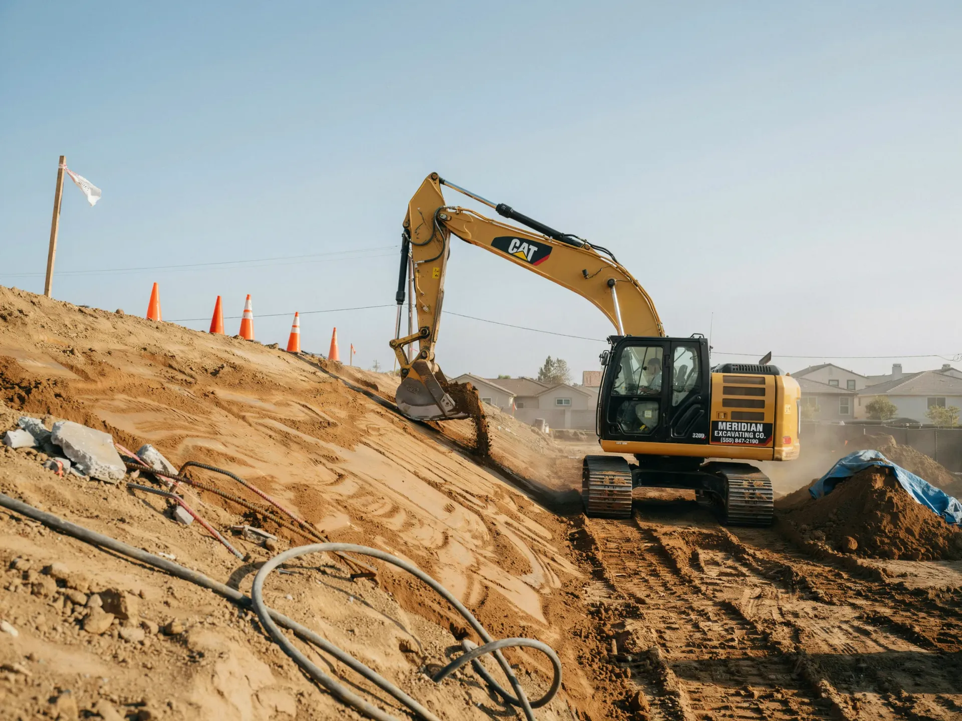 Yellow excavator digging on a sandy construction slope with orange cones and hoses nearby