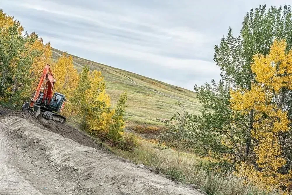 Person on an ATV riding along a dirt trail beside autumn trees and hills