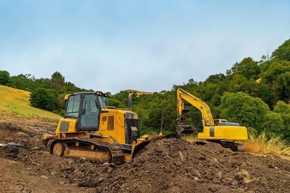 Two yellow excavators working on a muddy hillside under a blue sky