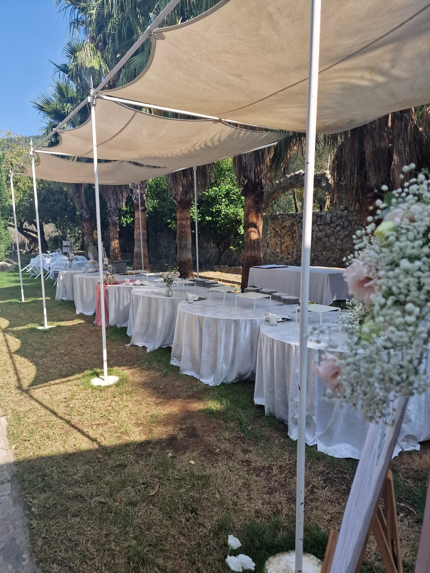 fila di tavoli bianchi sotto una tettoia sull'erba.