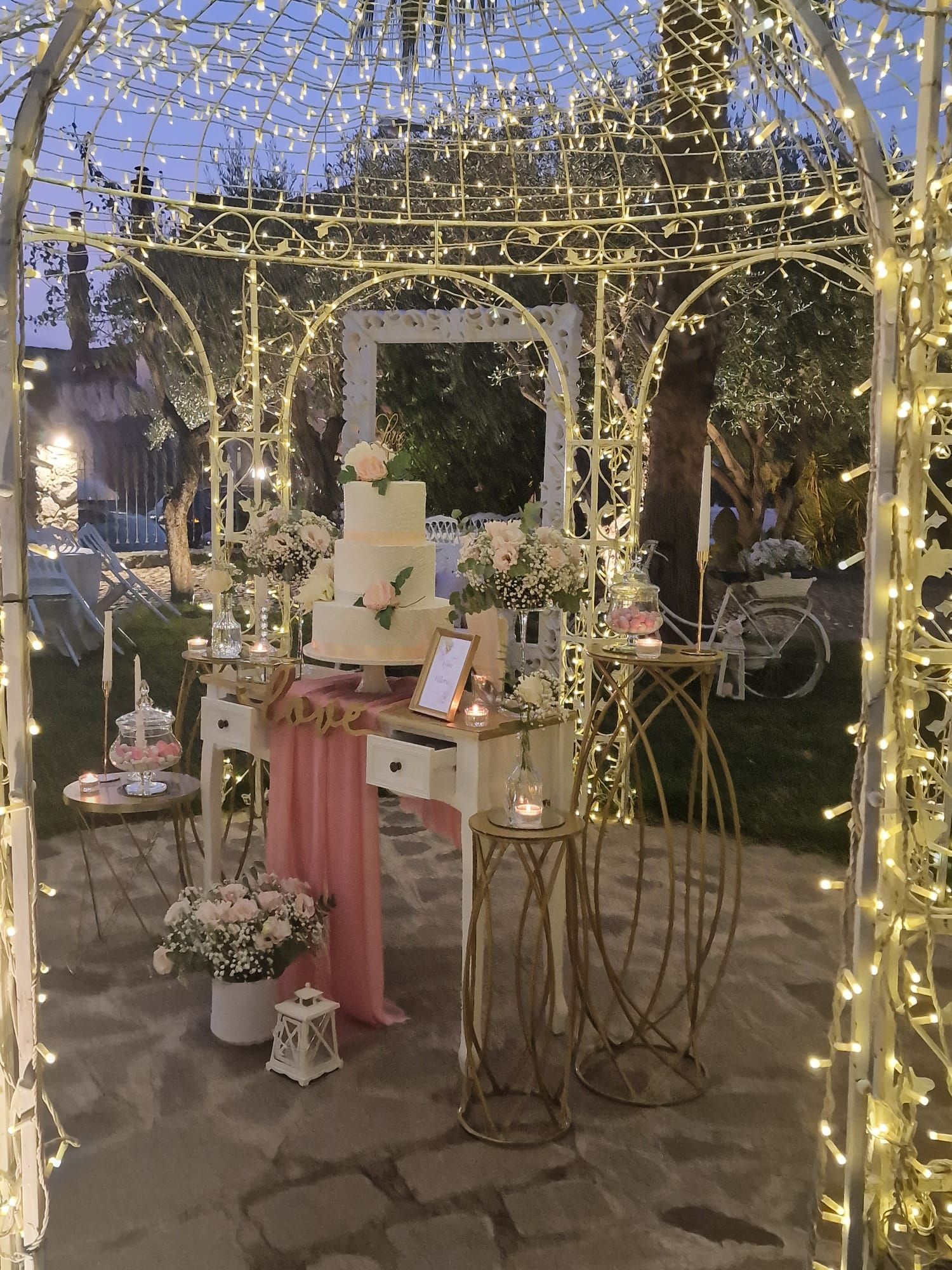 tavolo con una torta e dei fiori sotto un gazebo con delle luci