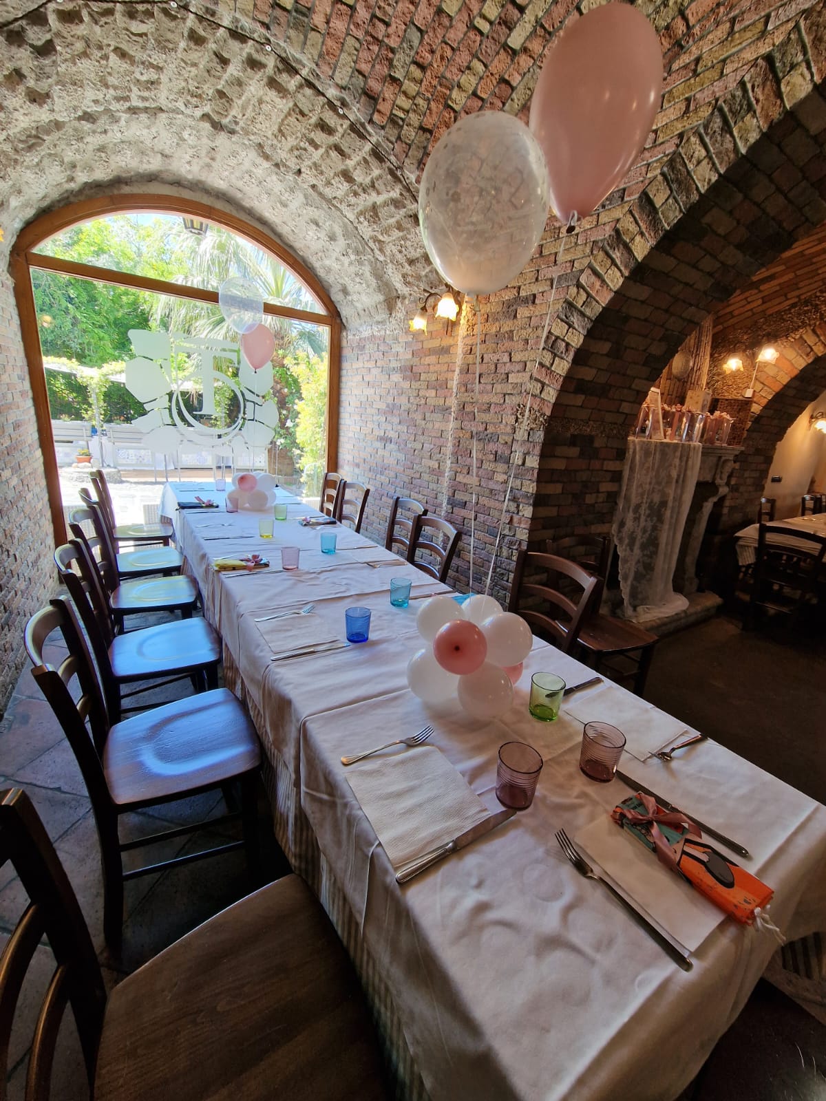 lungo tavolo con dei palloncini sopra in una stanza con un muro di mattoni