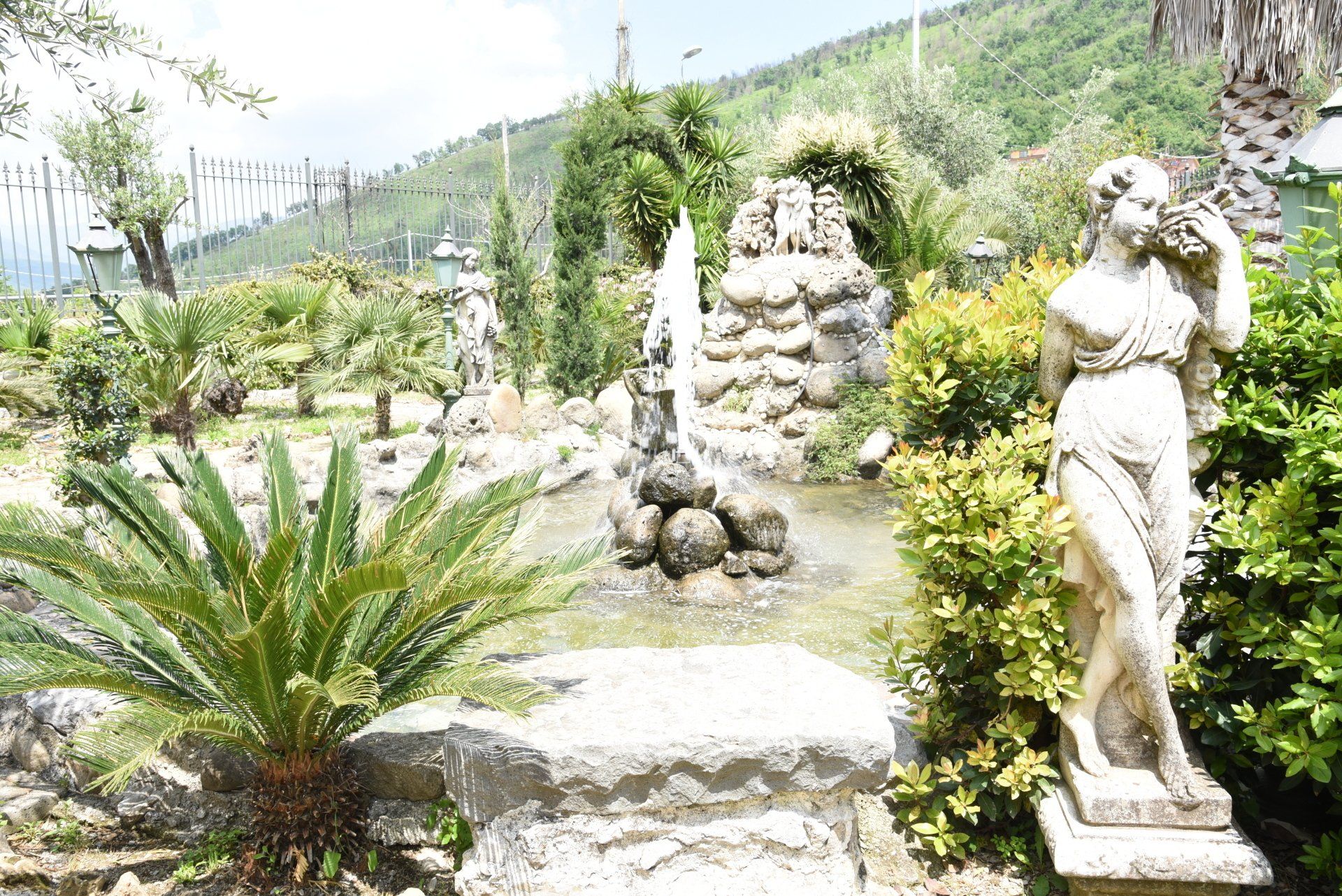 statua di una donna in piedi accanto a una fontana in un giardino