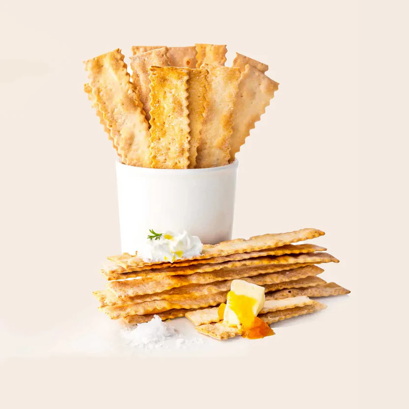 Crackers in a white cup, stacked with cheese, sour cream, and salt on a beige background.