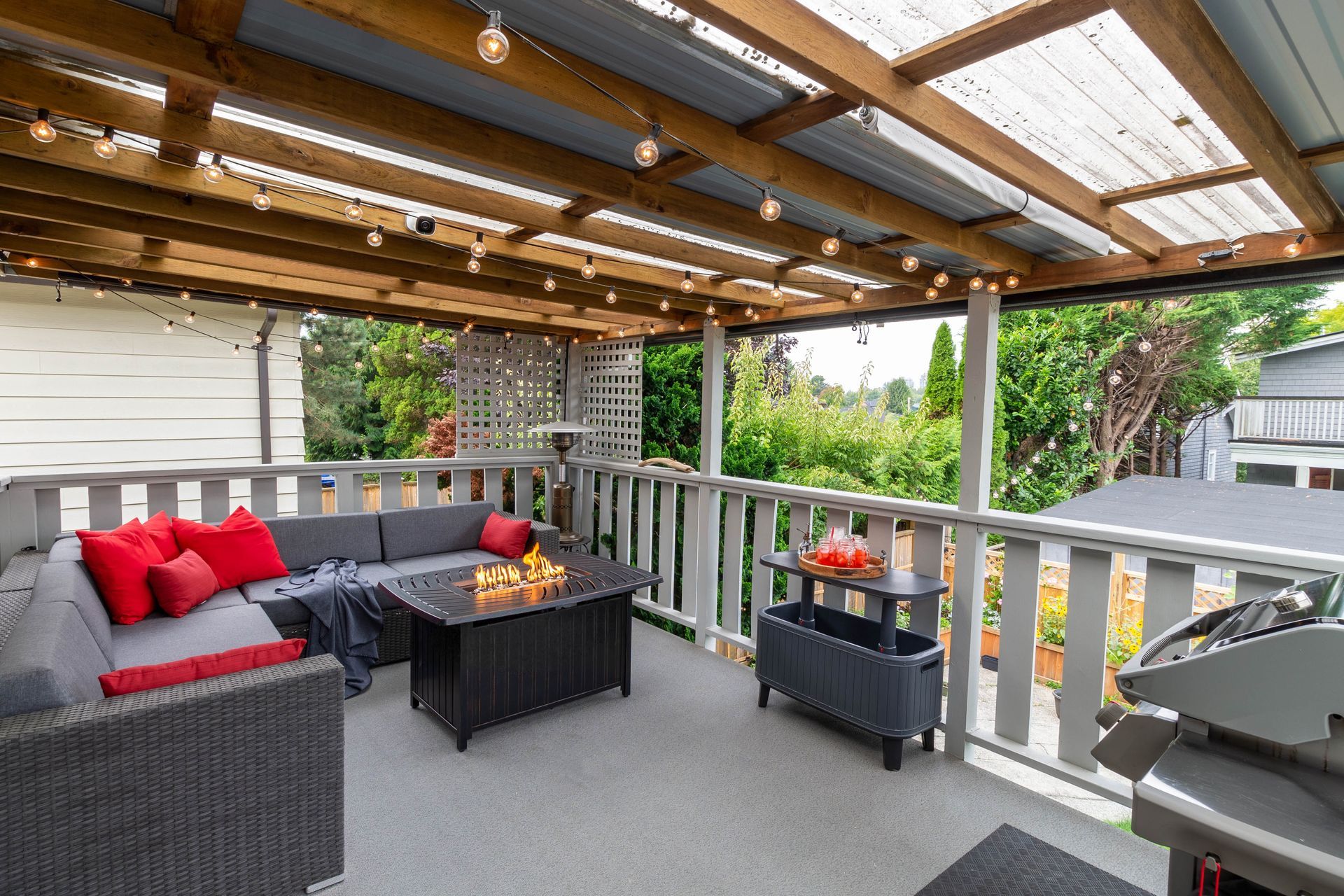 Covered outdoor deck with seating, string lights, and grill; overlooking a green backyard.