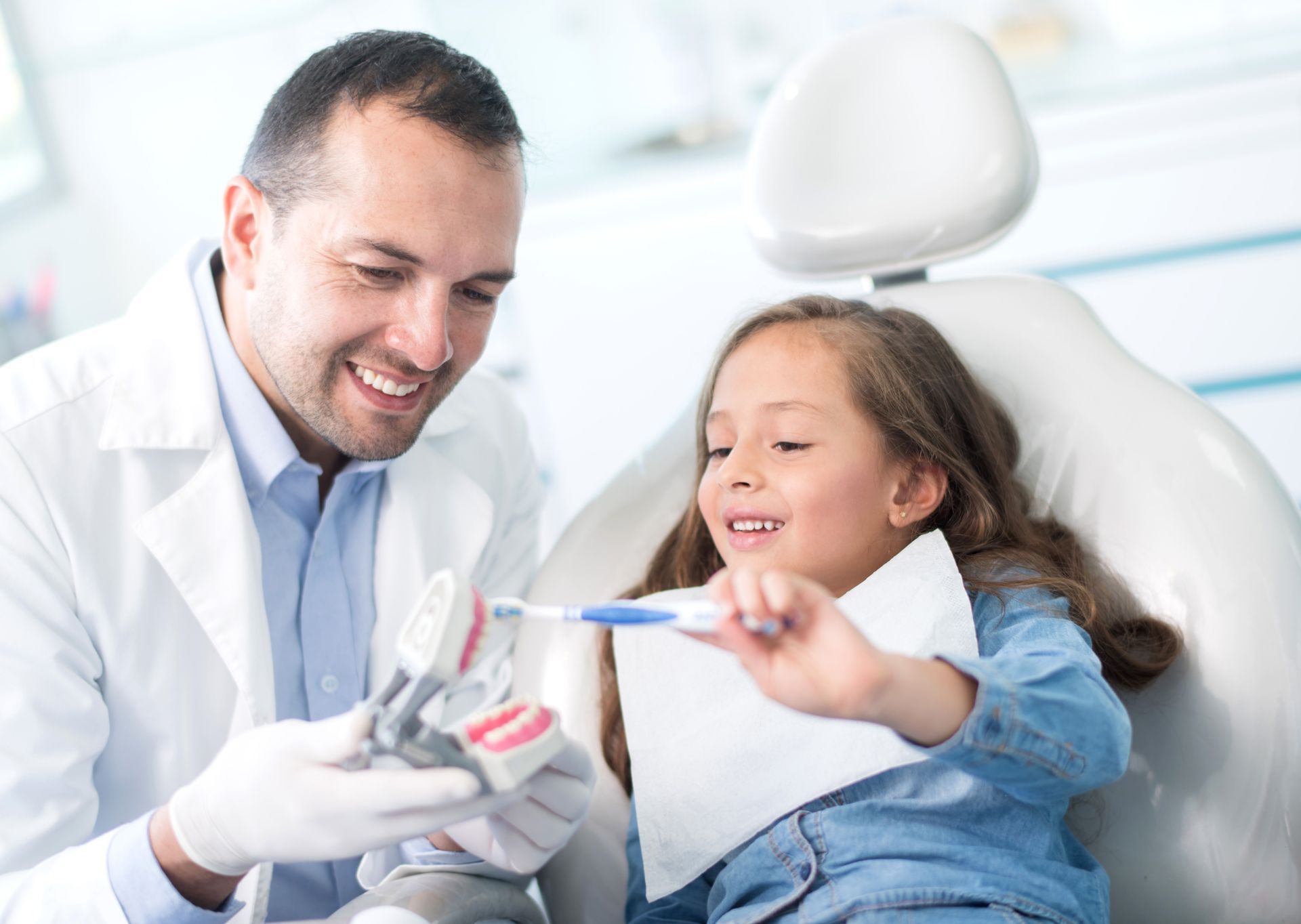 Young girl learning to brush teeth correctly using a denture at the dentist’s office.