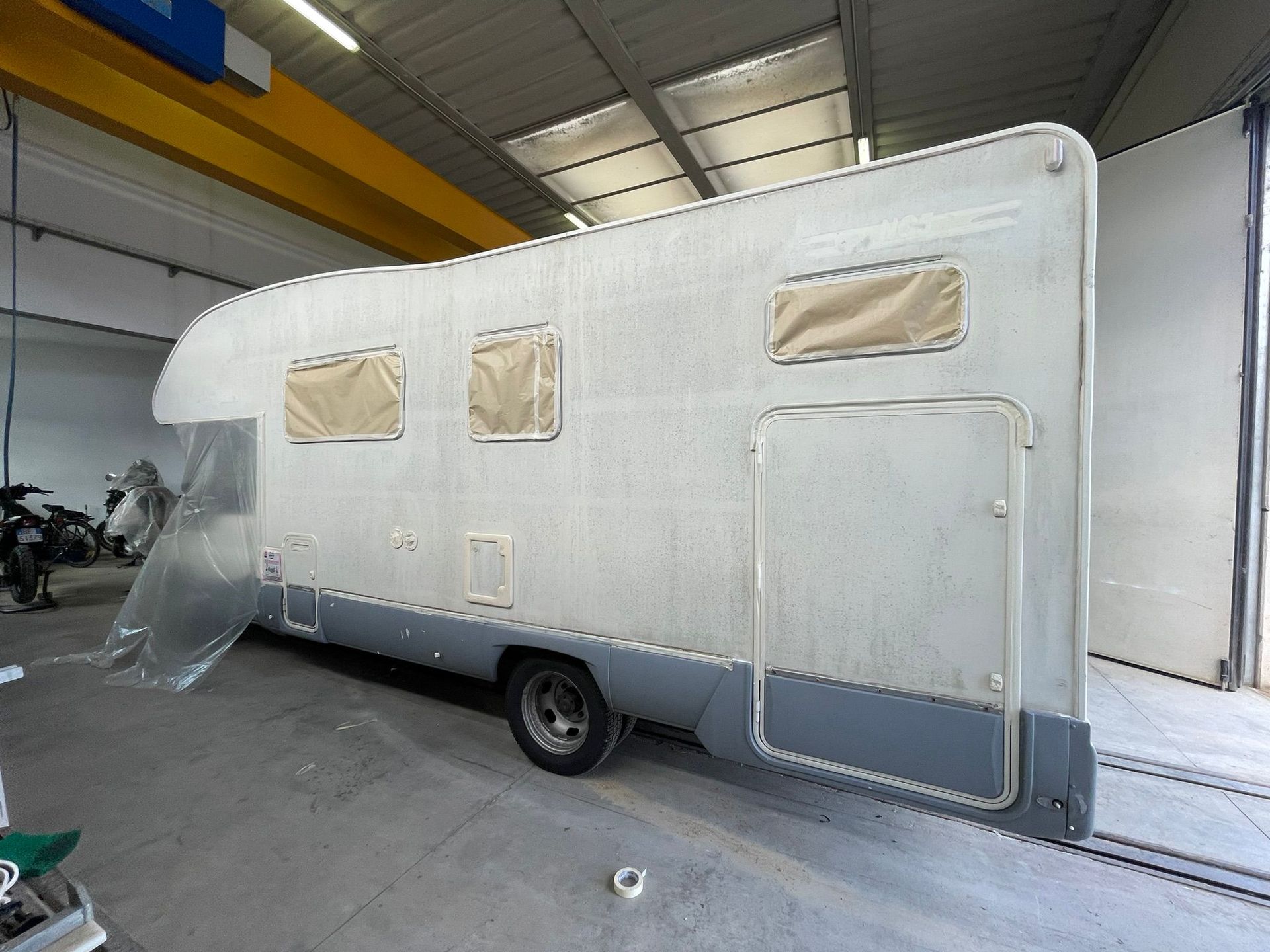 Camper in garage, in preparazione per la verniciatura. Esterno grigio e beige.