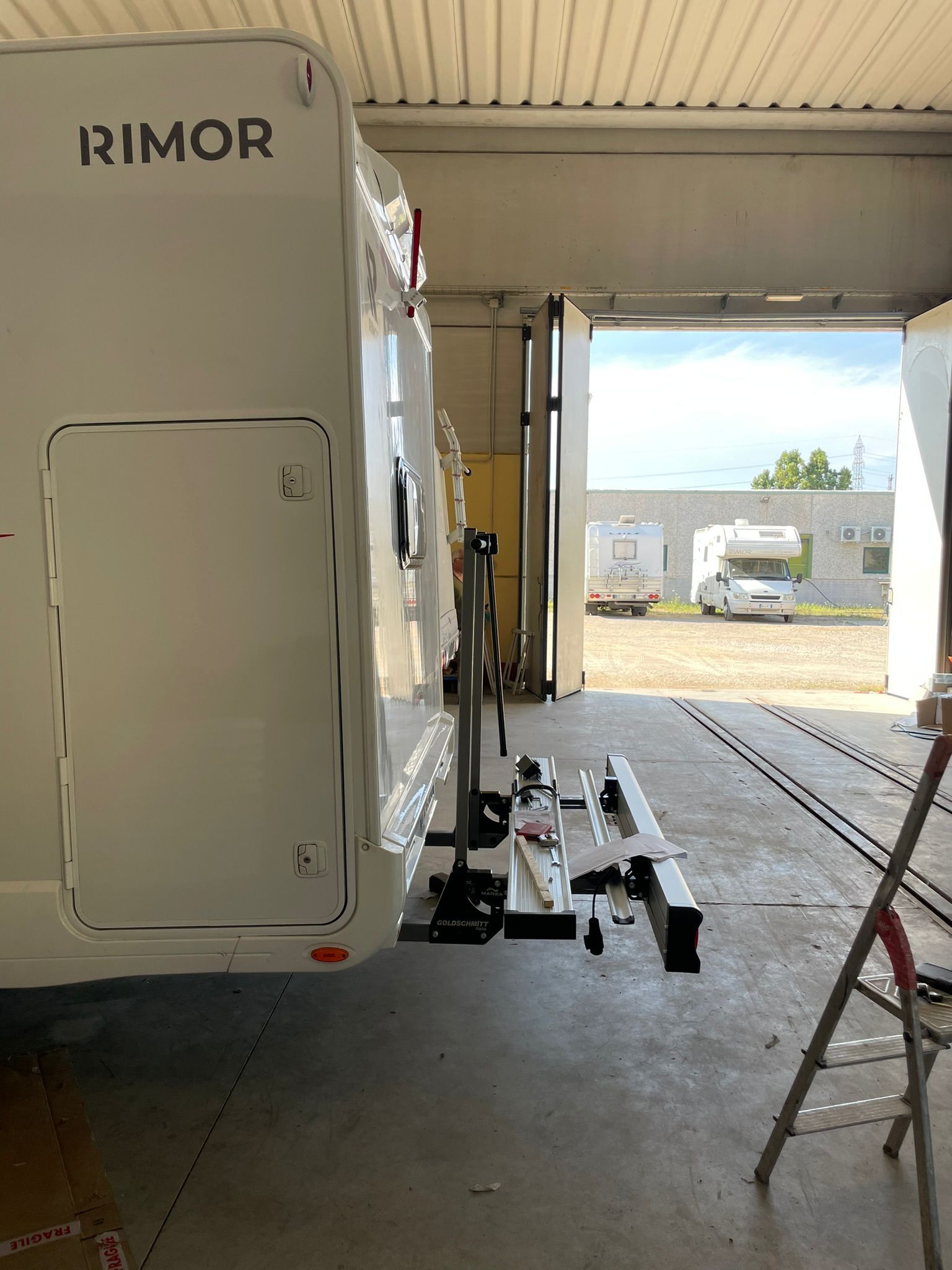Camper bianco con portabiciclette all'interno di un garage, vista attraverso la porta aperta.