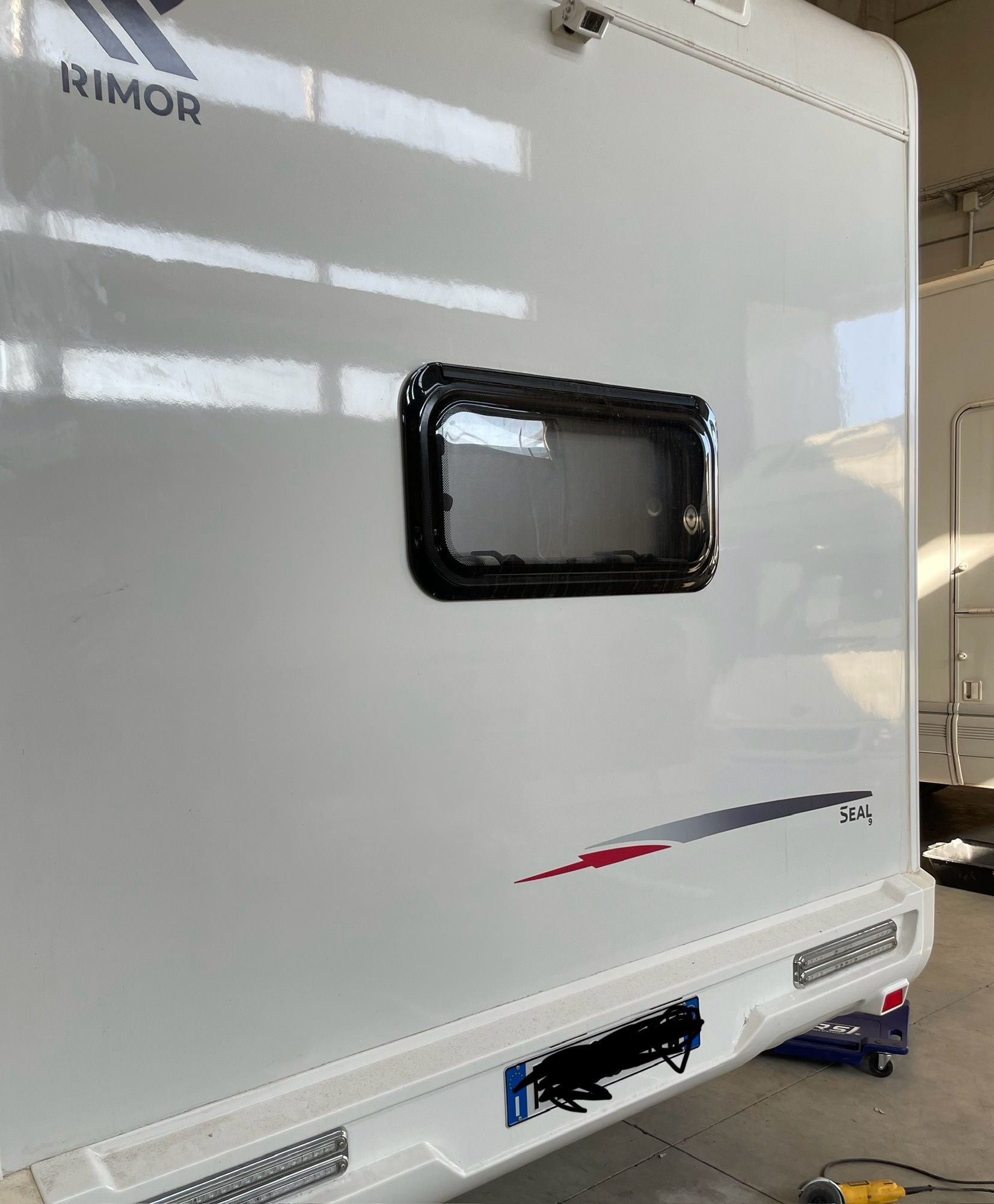 Parte posteriore bianca del camper con finestra, telaio nero e striscia decorativa rossa/grigia.