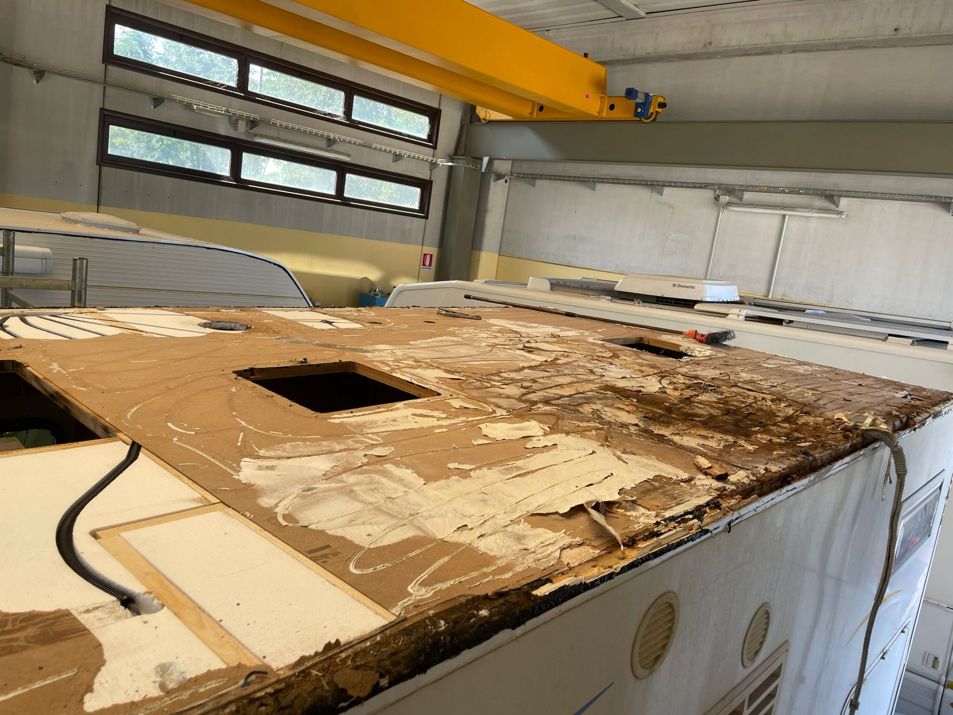 Tetto di un camper danneggiato in un'officina, con legno esposto e sezioni mancanti.