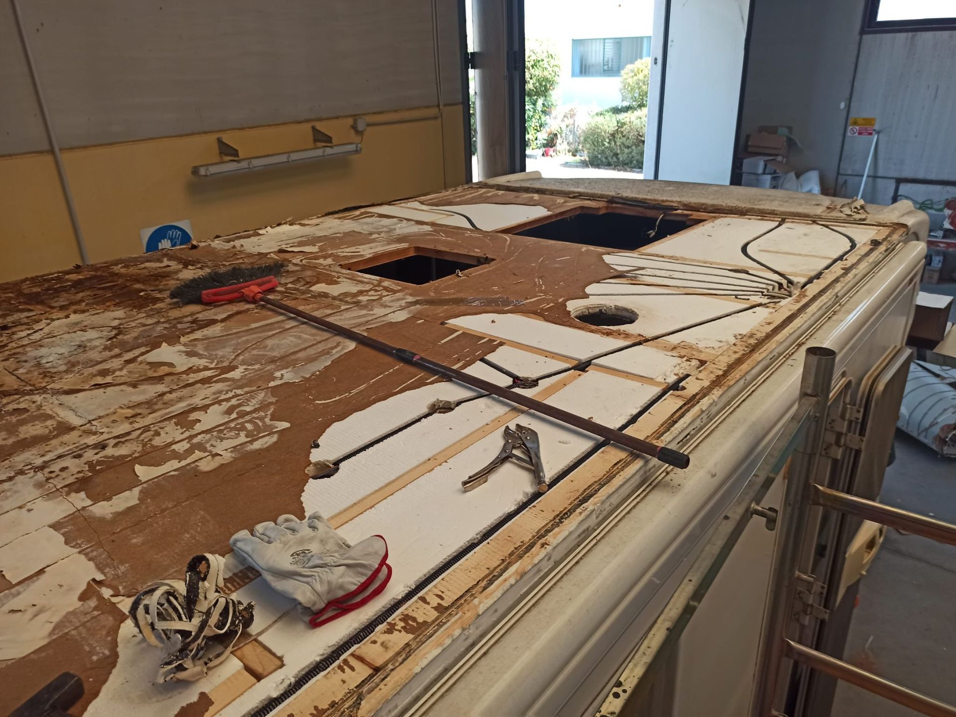 Tetto di un camper in riparazione, con sezioni rimosse che espongono il compensato, attrezzi appoggiati sulla superficie.