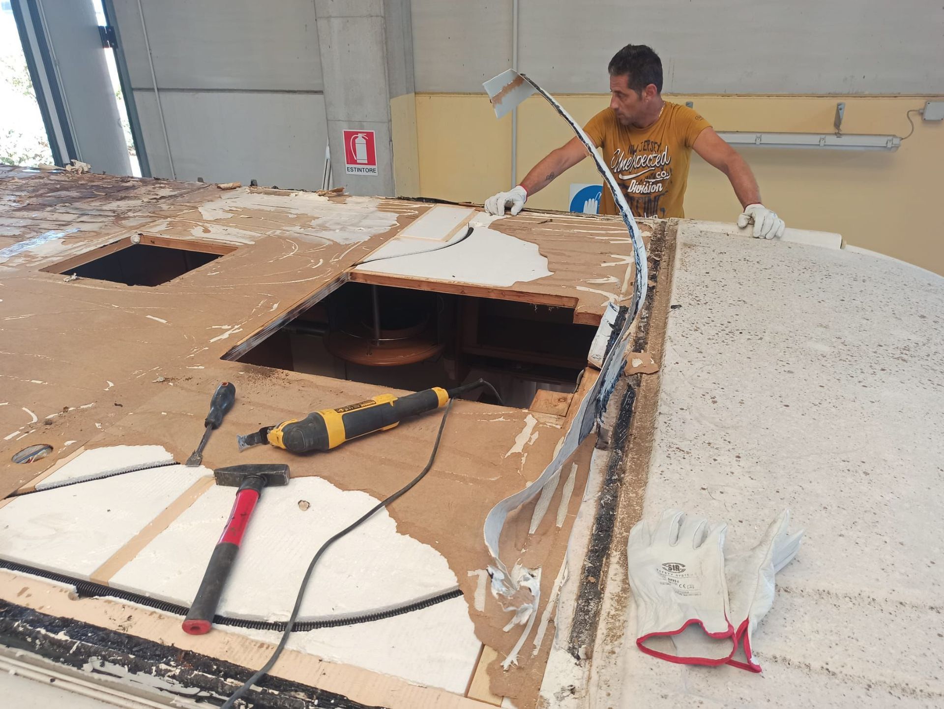 Un uomo ripara il tetto di una barca. Sta usando degli attrezzi in un'officina.