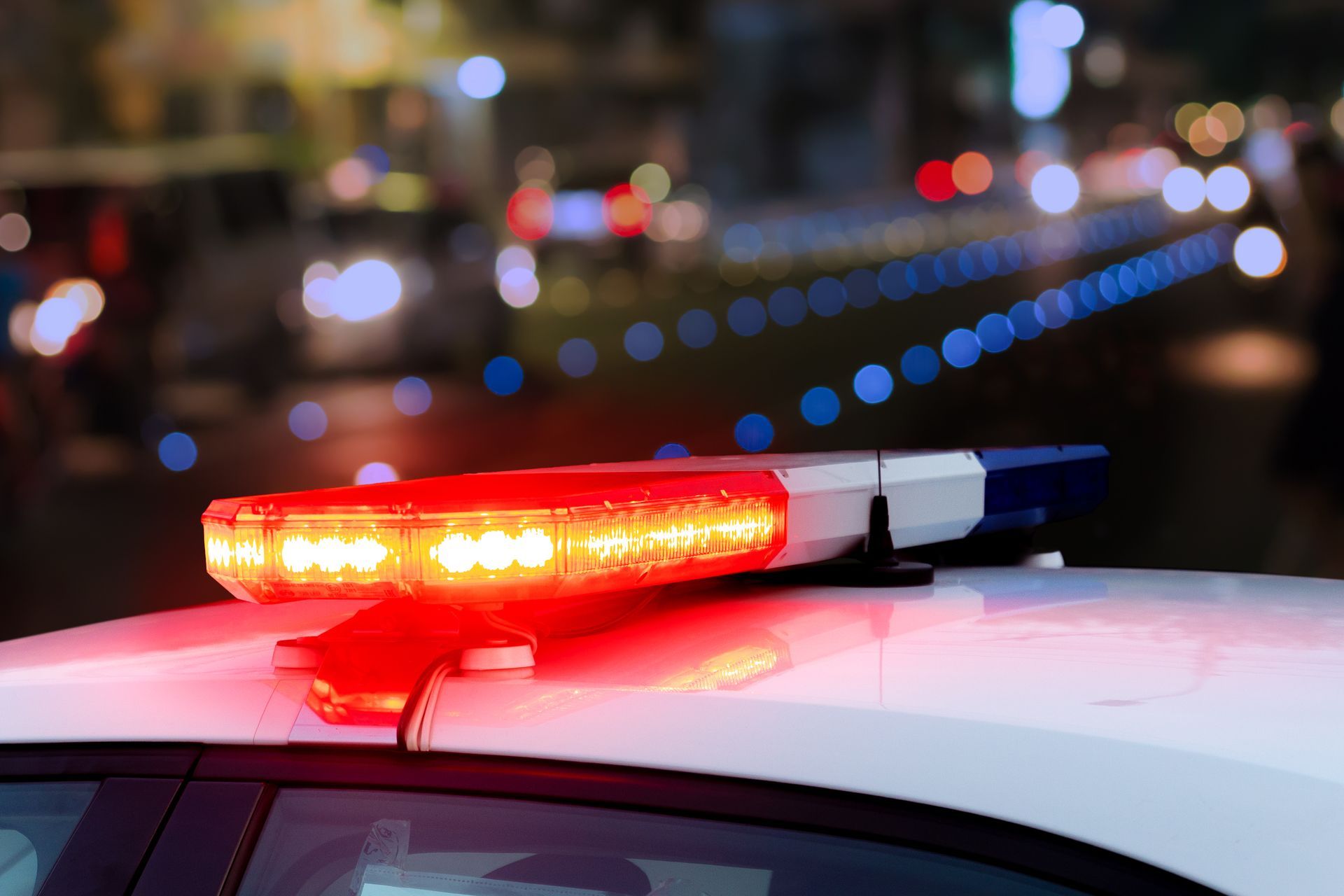 Police car with flashing red and blue lights, night setting, blurred city lights in background.
