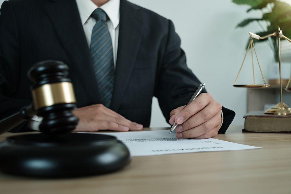 Lawyer in suit writing at desk, gavel and scales of justice present.