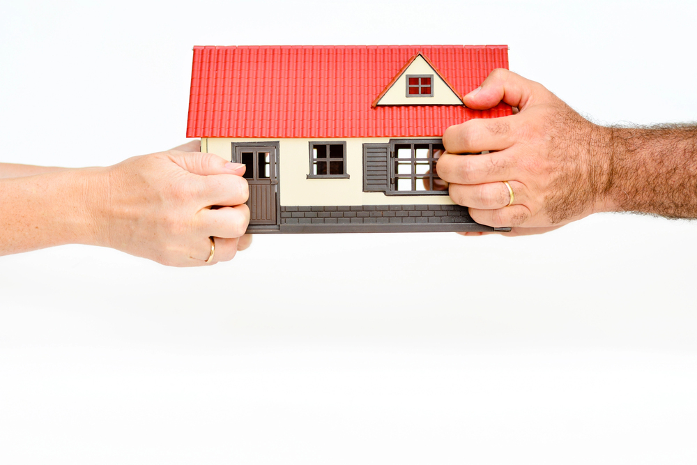 Hands of two people holding a toy house, symbolizing property division.