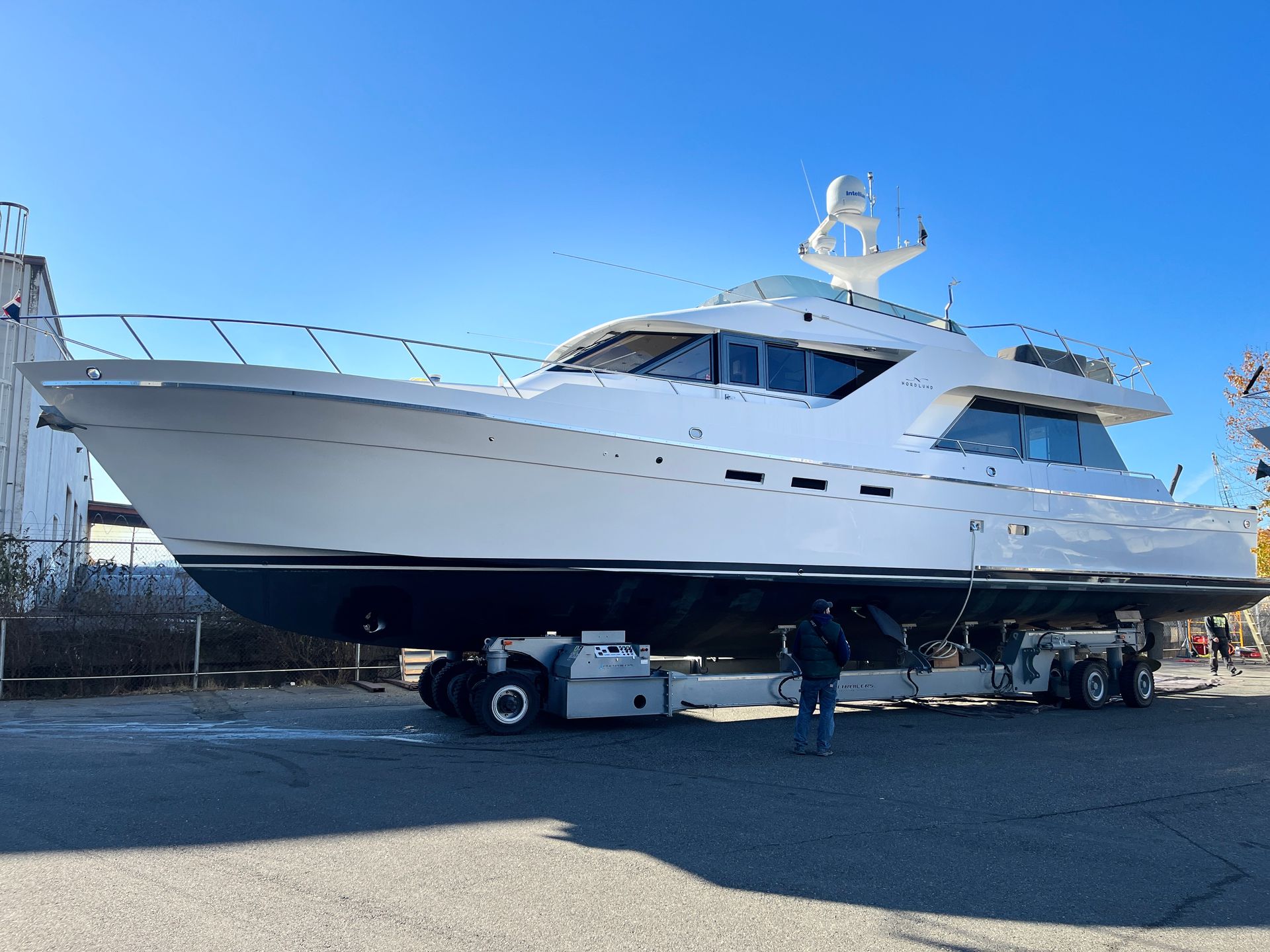A large white boat is on a trailer in a parking lot.