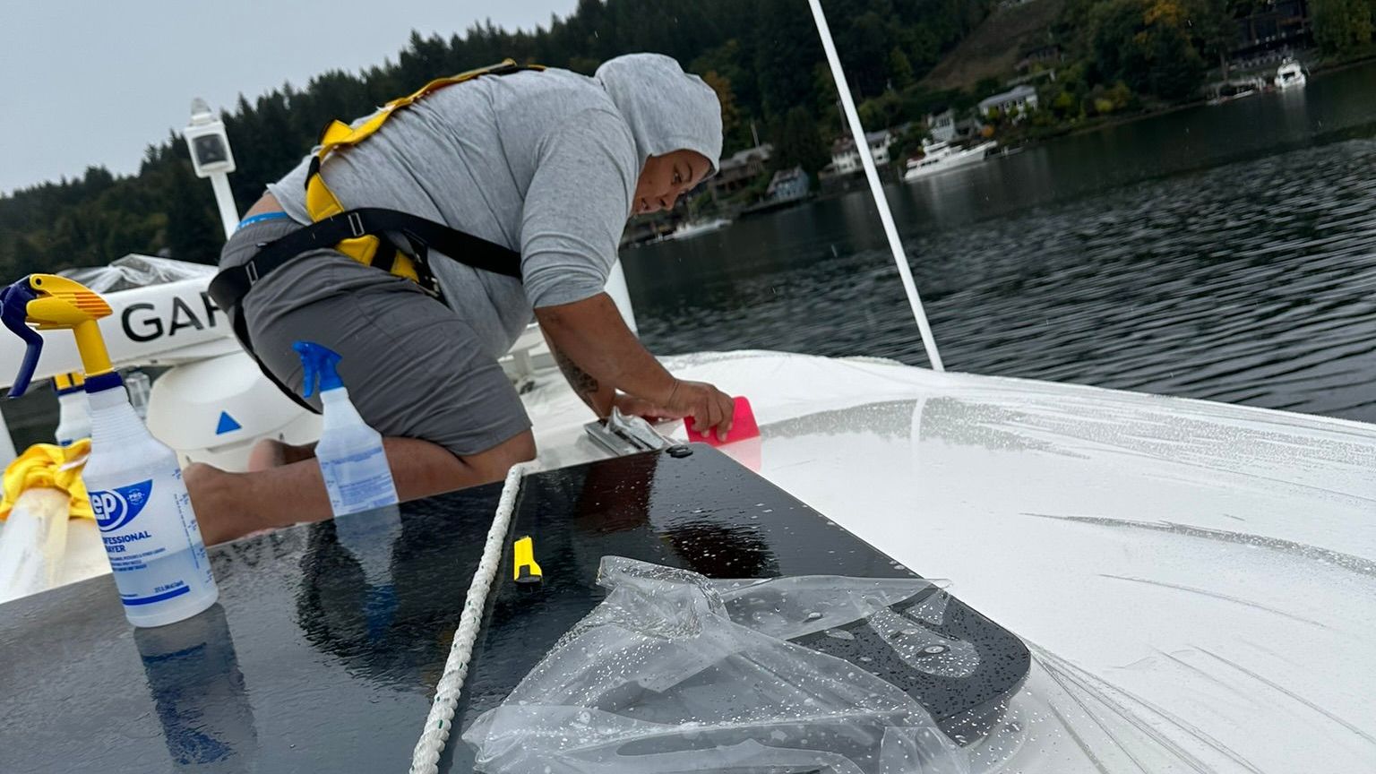 A man is cleaning the roof of a boat in the water.