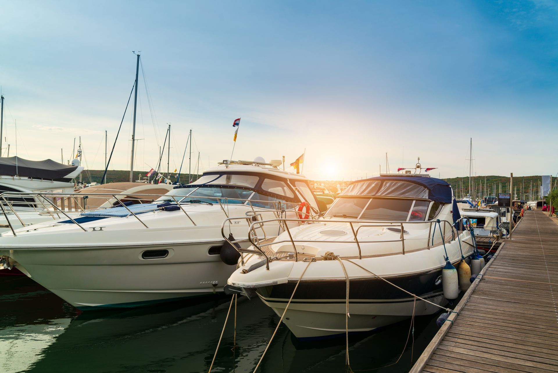 A row of boats are docked in a marina at sunset.