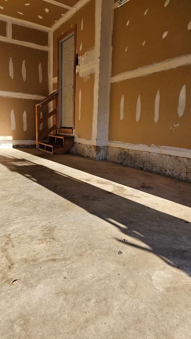 Garage interior with concrete floor, drywall walls, door, and small wooden steps. Long shadow crosses floor.