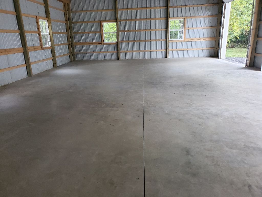 Empty concrete floor inside a metal building with insulation and windows.