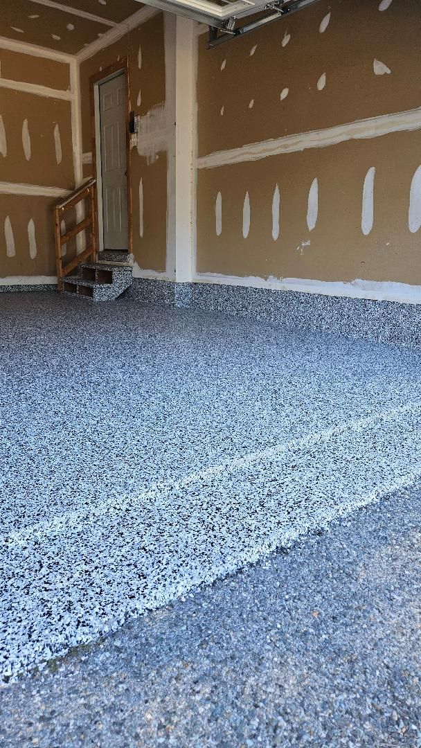 Garage interior with a newly installed speckled floor, unfinished walls, and an open doorway.