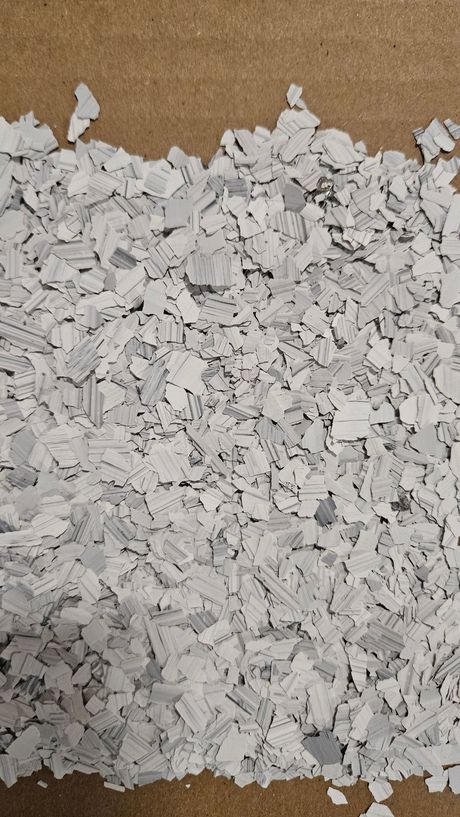 Gray and white floor flakes scattered on a brown surface.