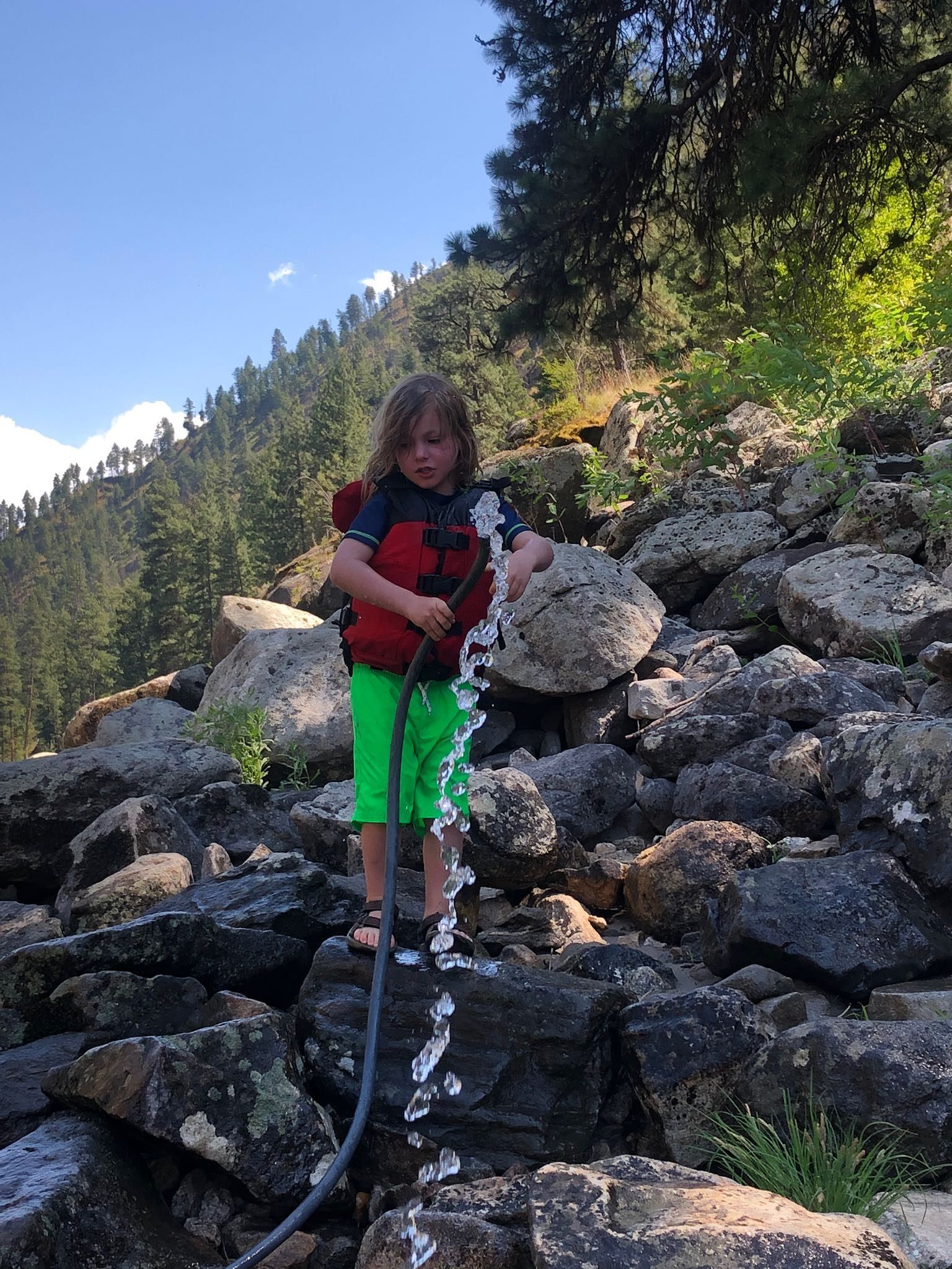 A young boy is standing on a rocky hill holding a hose.