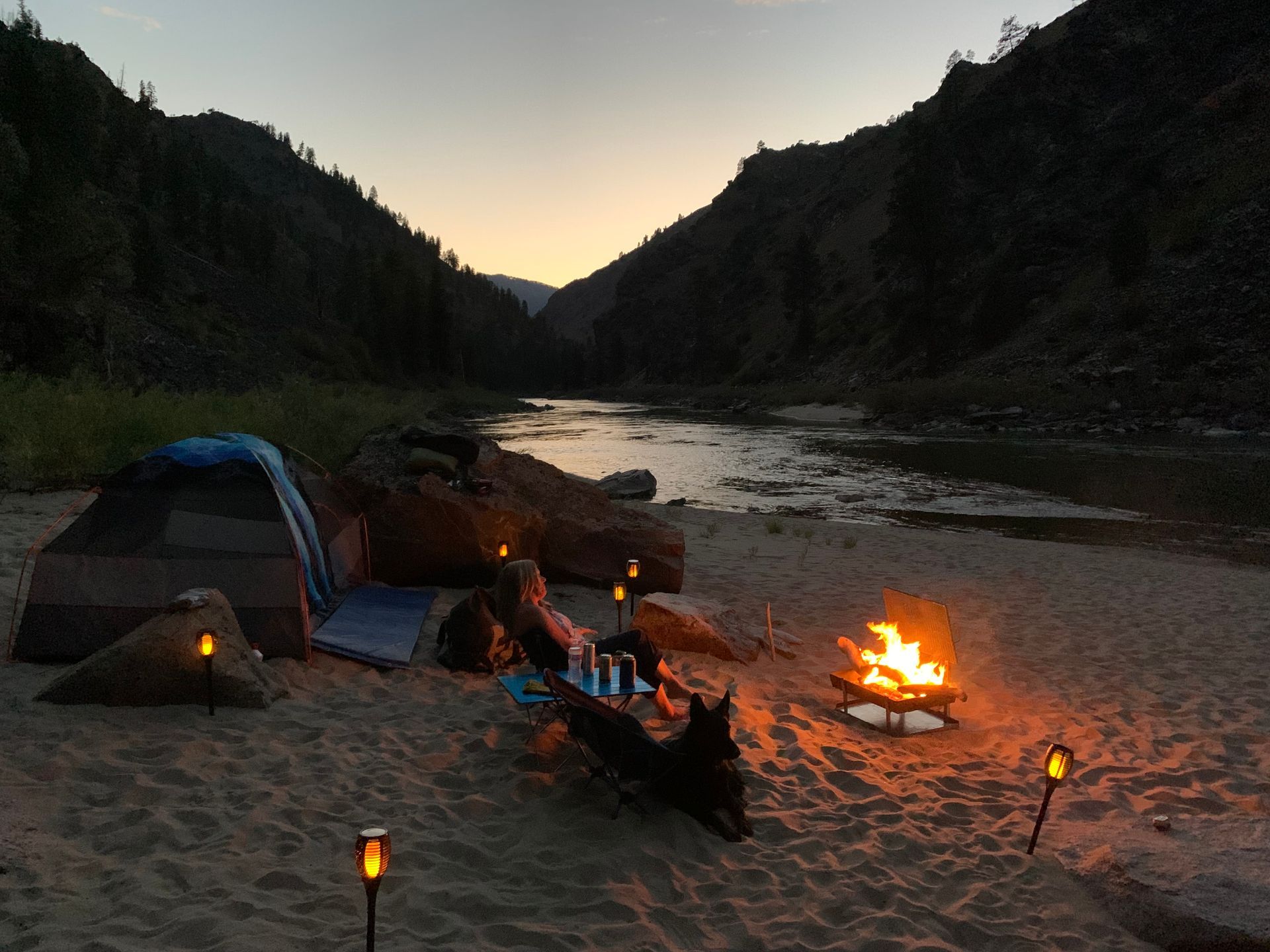 A campfire is lit up on the beach near a river.