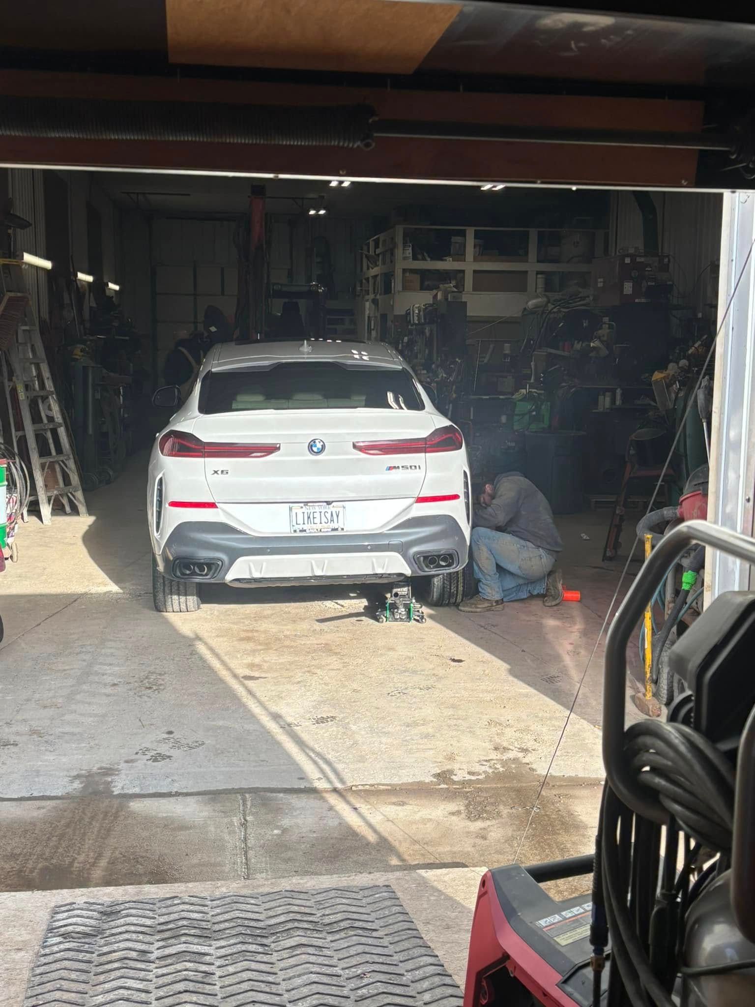 A white car is parked in a garage with a man working on it.