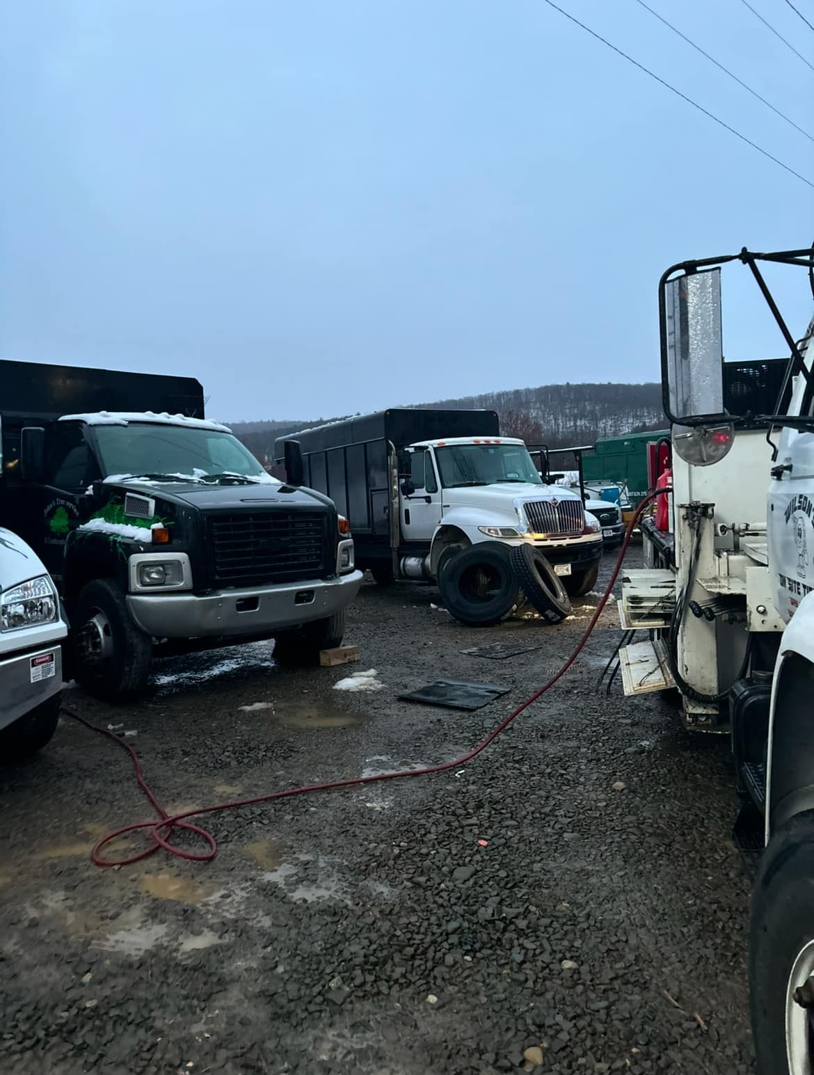 A row of trucks are parked in a gravel lot.