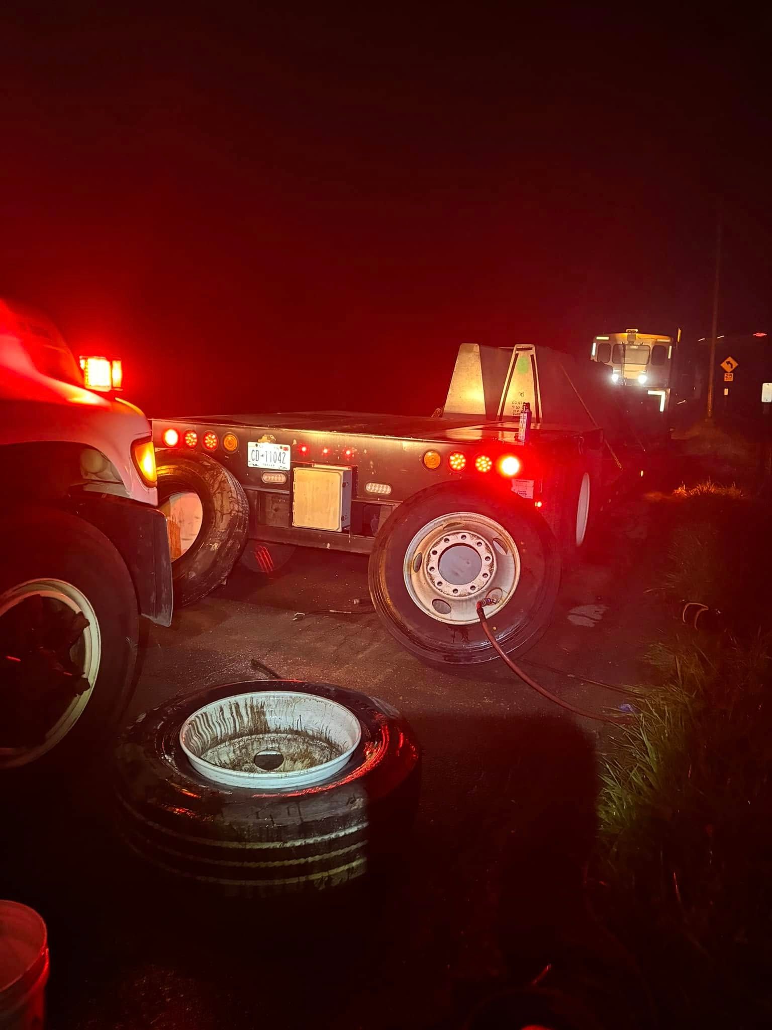 A truck with a flat tire is sitting on the side of the road at night.